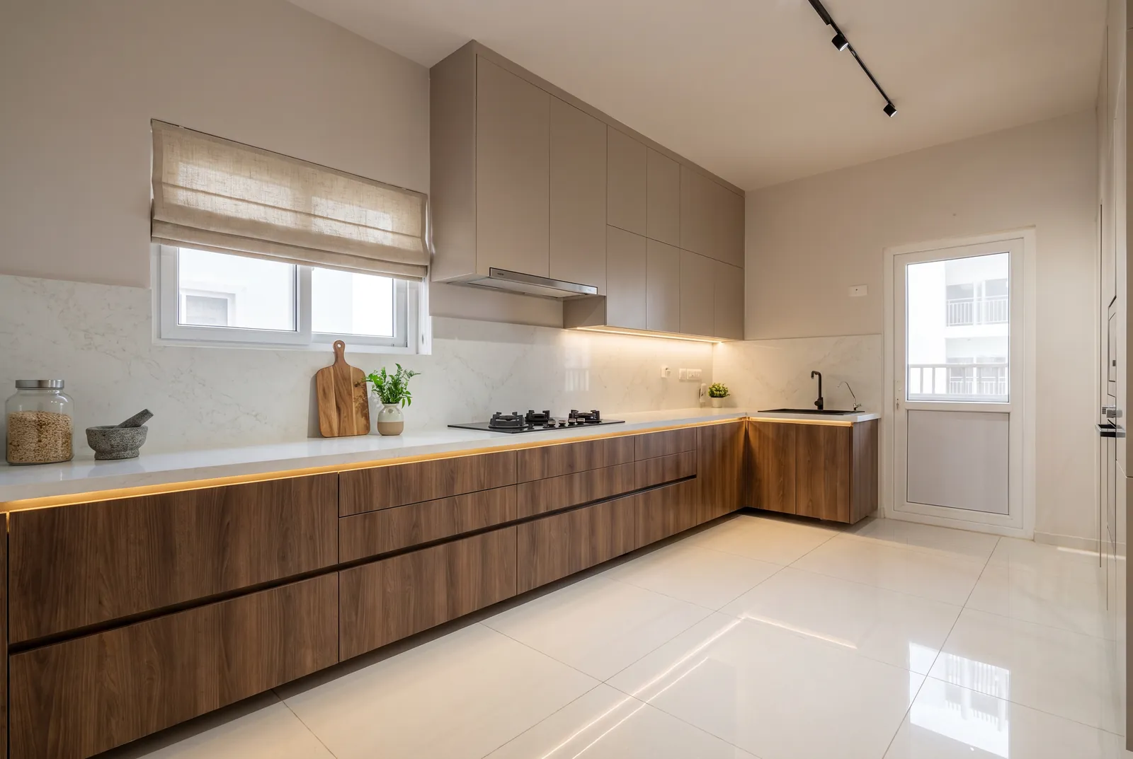 A galley kitchen with wood-grain base cabinets, taupe wall cabinets and a linen blind.