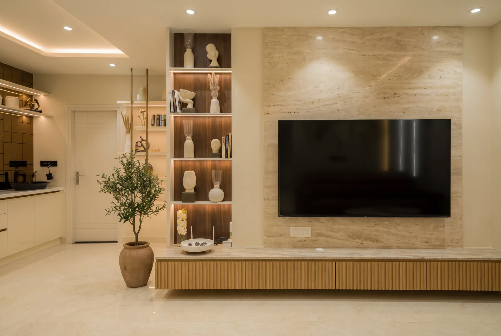 A TV wall in honed travertine with lit walnut niches and a fluted oak console.