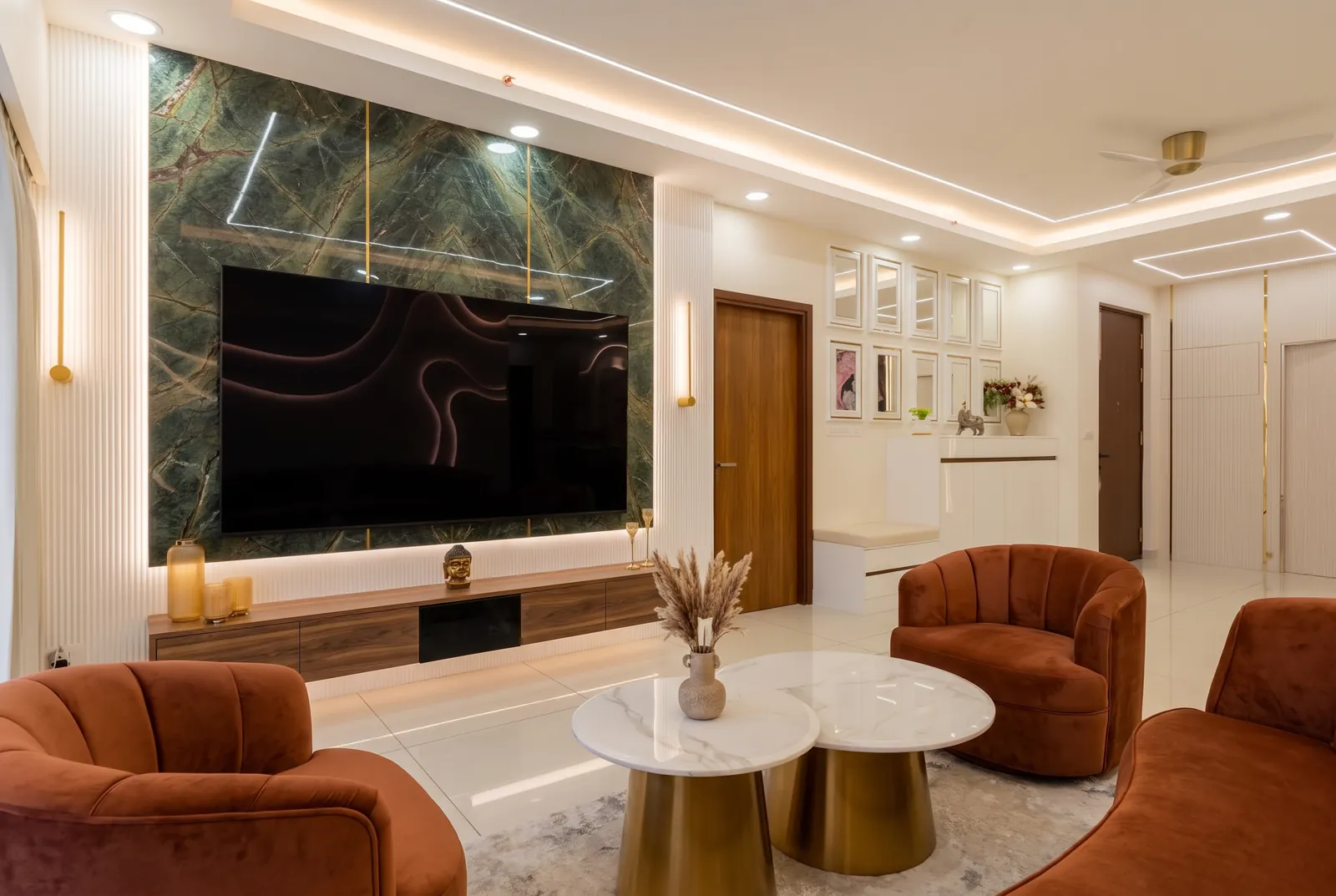 A living room with a green marble TV wall, a walnut console and rust velvet armchairs.