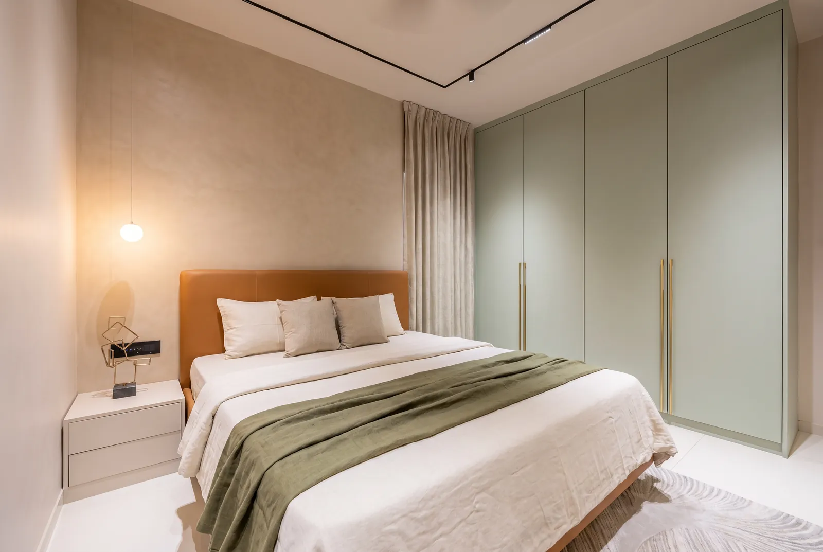 A bedroom with hinged sage-green matt wardrobes with long brass pulls.