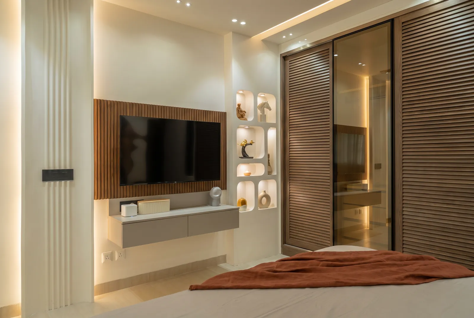 A sliding wardrobe in slatted oak with a bronze-glass door beside a TV wall in fluted walnut.
