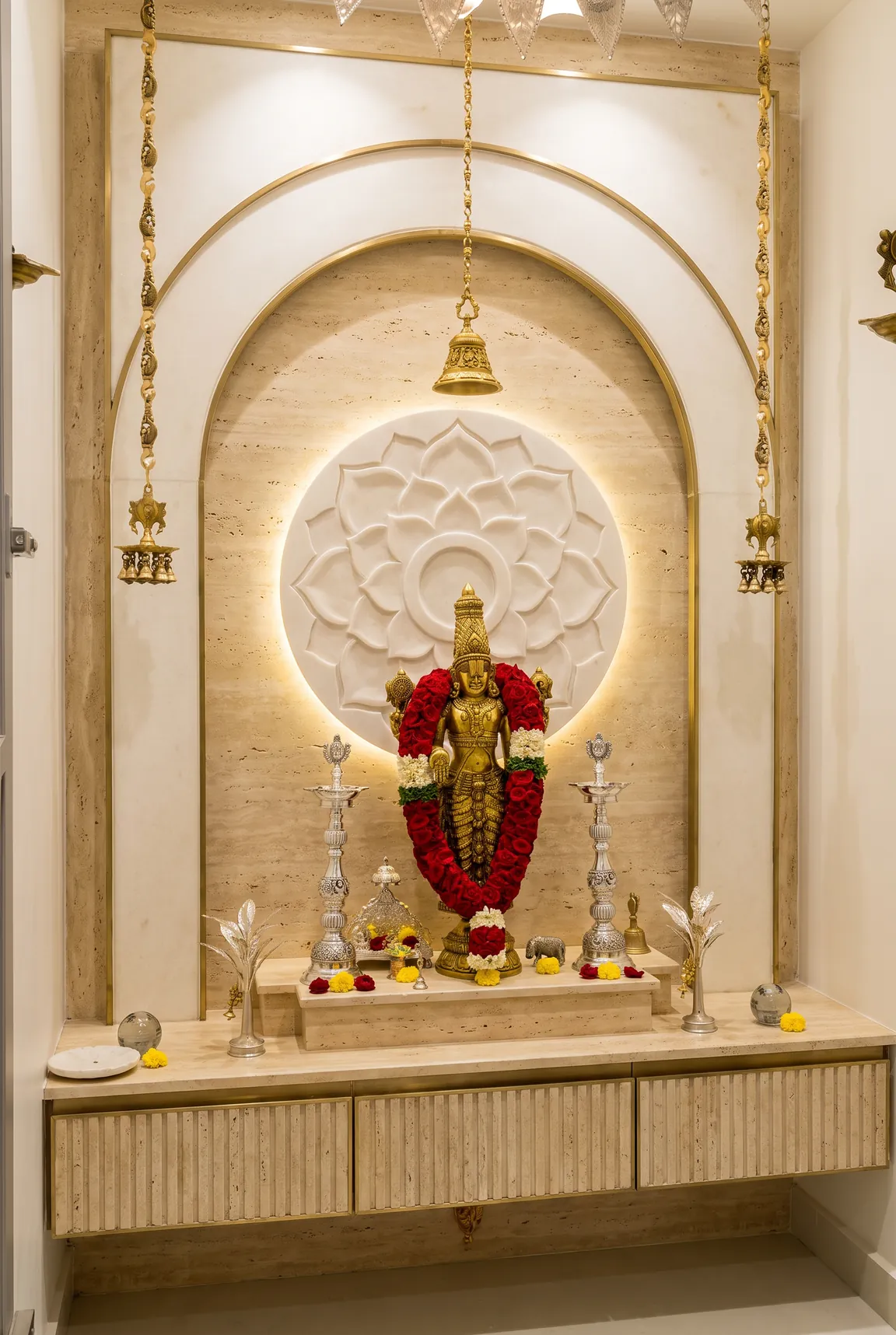 A pooja unit in travertine with a backlit lotus medallion, brass lamps and marigold garlands.